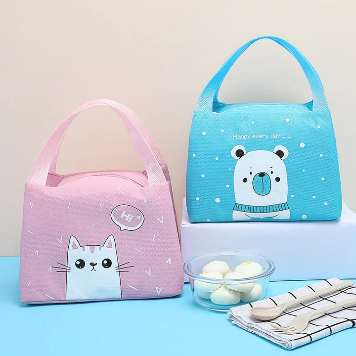 Pink cat and blue bear design lunch bags with handles, displayed with a bowl of dumplings and wooden cutlery on striped napkin