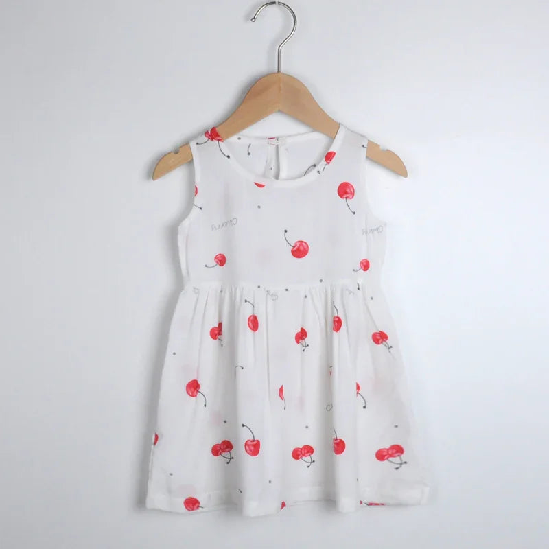 White sleeveless toddler dress with red cherry print on a wooden hanger against white wall