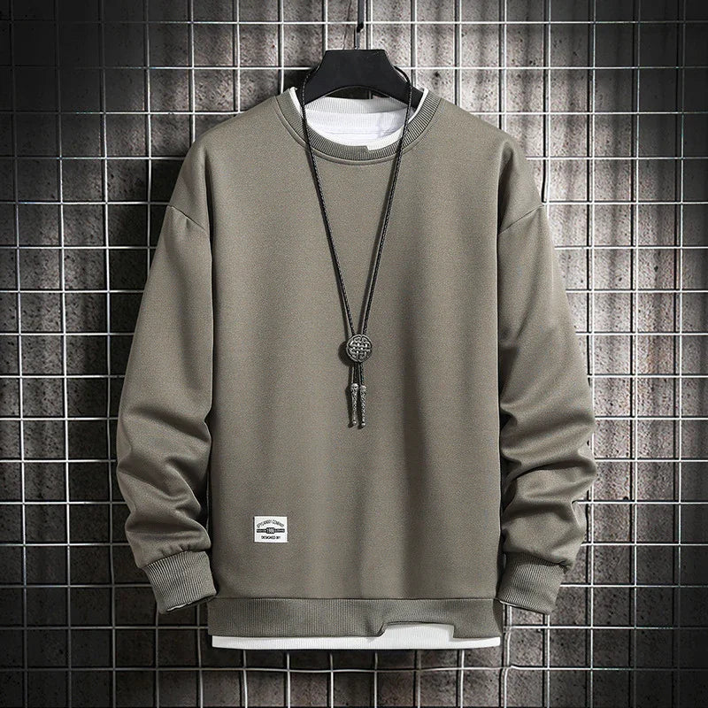 olive green casual sweatshirt with ribbed cuffs and hem, layered over white shirt, displayed on hanger with pendant necklace