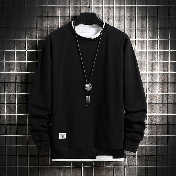 Black long-sleeve sweatshirt layered over white shirt with pendant necklace on hanger against metal grid wall