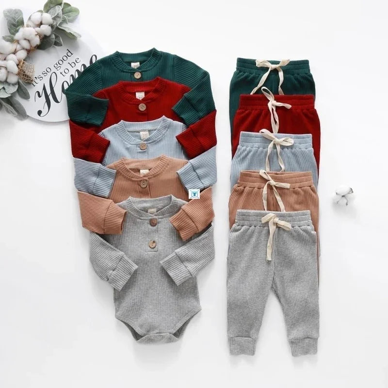 Set of ribbed knit baby bodysuits and matching pants in green, red, blue, beige, and gray on white background with cotton decor
