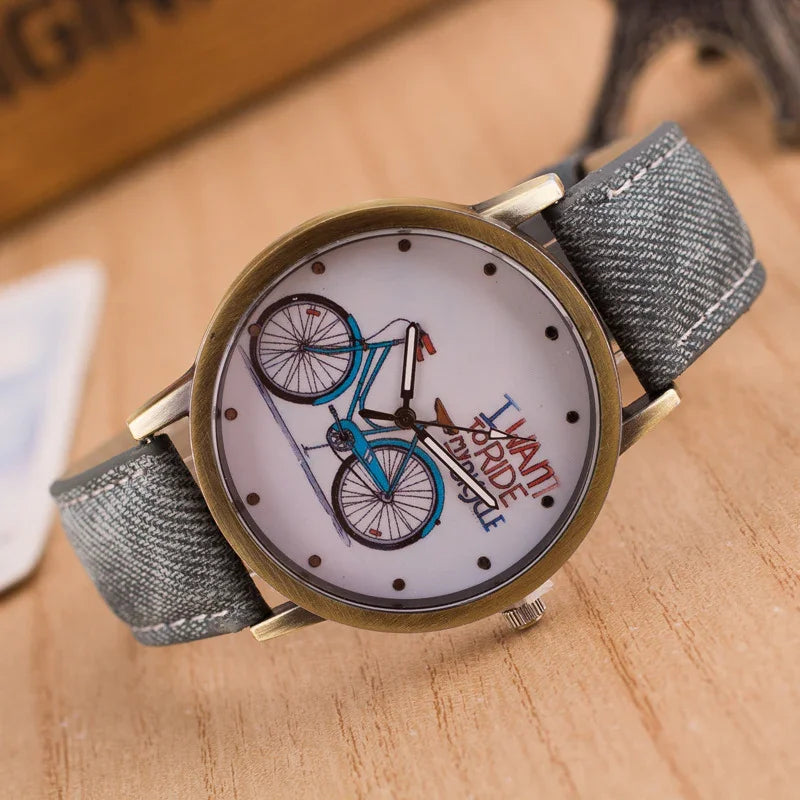 Close-up of wristwatch with blue bicycle design and 'I want to ride my bicycle' text on white dial and grey fabric strap