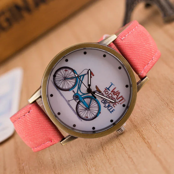 Close-up of wristwatch with red strap featuring blue bicycle illustration and text 'I want to ride bicycle' on white dial