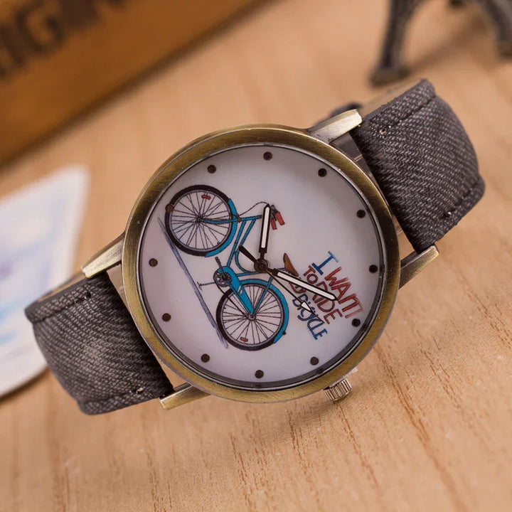 Round wristwatch with a blue bicycle illustration and text I want to ride my bicycle on the dial, black fabric strap