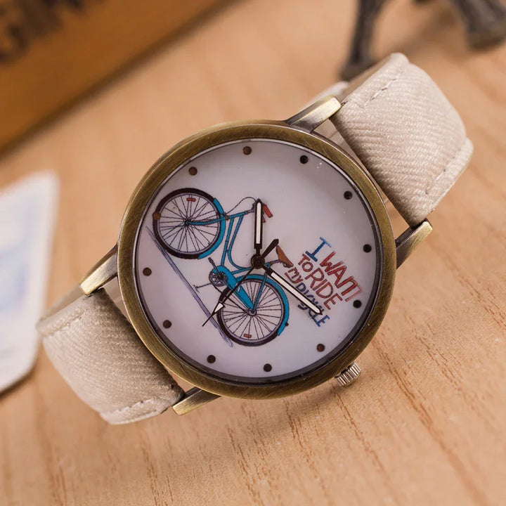 Close-up of wristwatch with beige fabric strap and bicycle design on white dial reading 'I want to ride my bicycle'