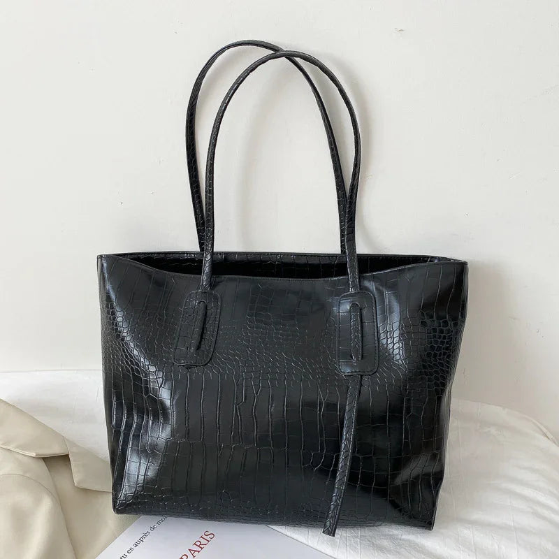 Black faux crocodile leather tote bag with double handles on white surface