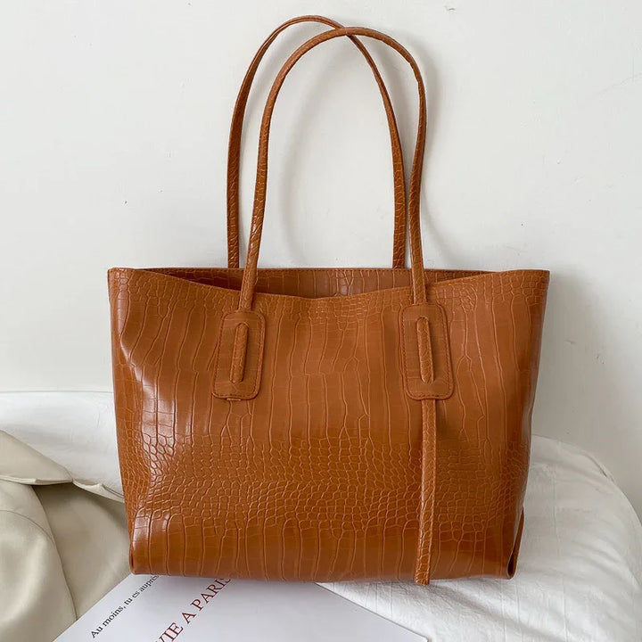Brown crocodile embossed leather tote bag with double handles on white surface