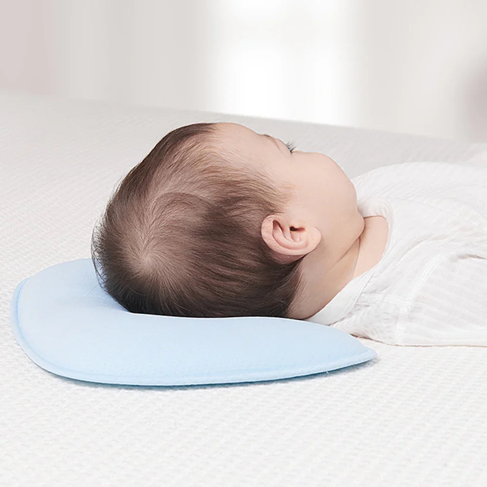 Baby lying on back with head resting on light blue infant pillow on white textured surface