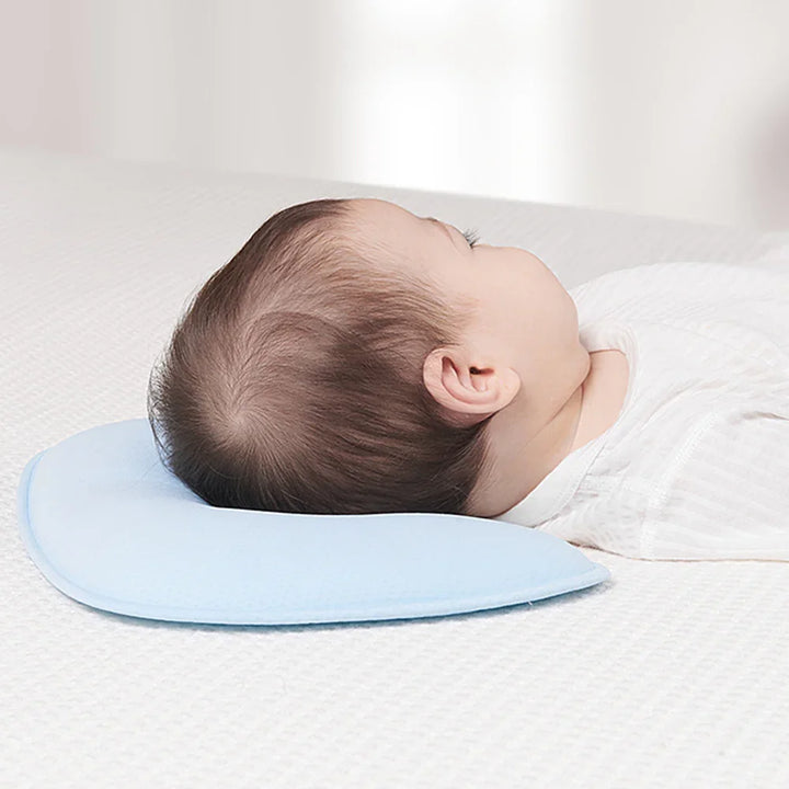 Baby lying on back with head resting on light blue infant pillow on white textured surface