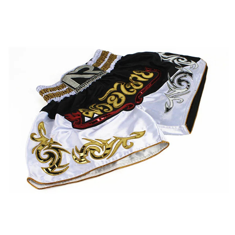 Black and white Muay Thai shorts with gold and silver tribal embroidery on white background