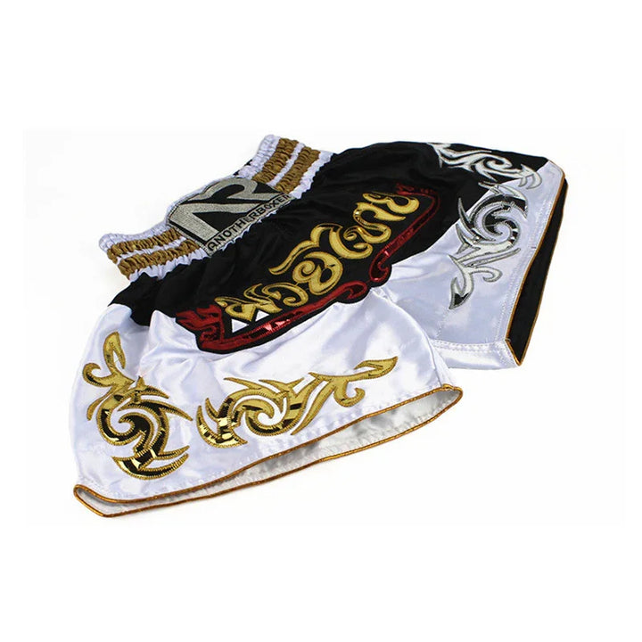 Black and white Muay Thai shorts with gold and silver tribal embroidery on white background