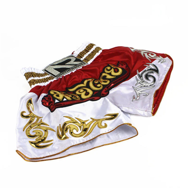 Red and white Muay Thai boxing shorts with gold embroidery and bold logo on waistband
