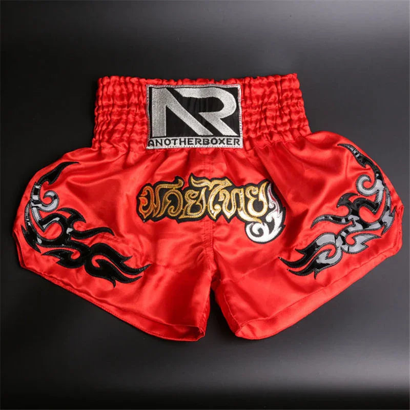 Red Muay Thai boxing shorts with gold Thai script, black tribal patterns, and AnotherBoxer logo