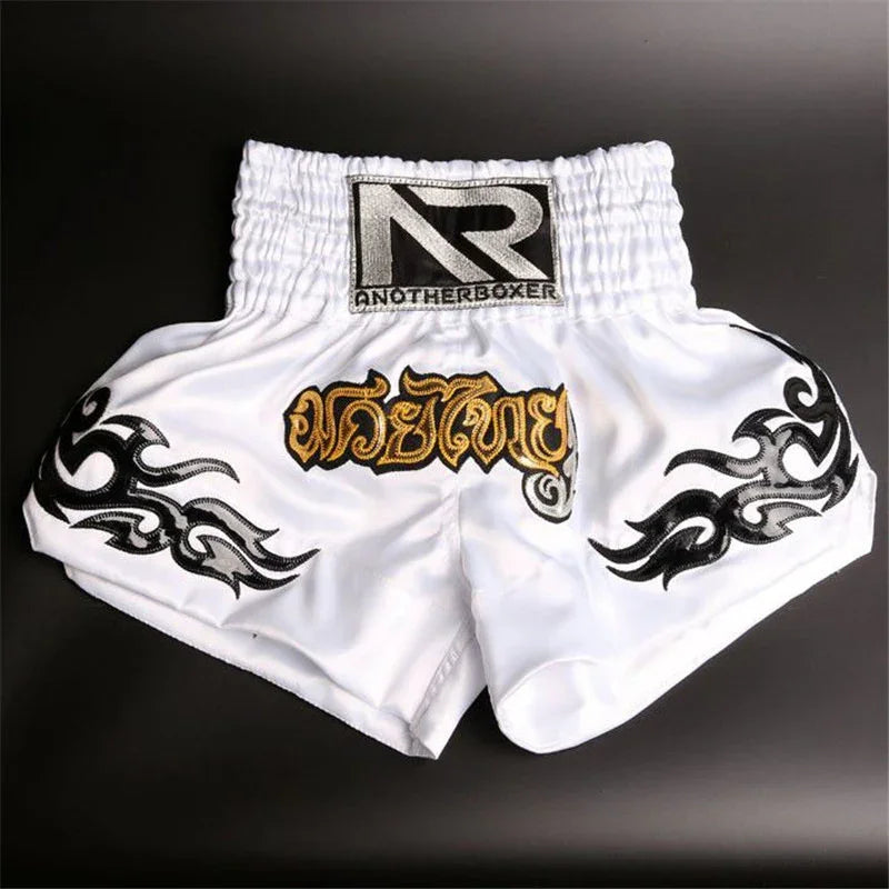 White Muay Thai boxing shorts with black tribal designs and gold Thai script on the front.