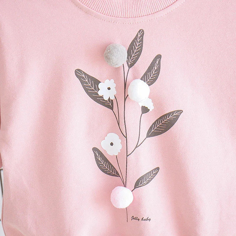 Pink sweatshirt with floral print, black leaves, white flowers, and 3D pom-pom accents