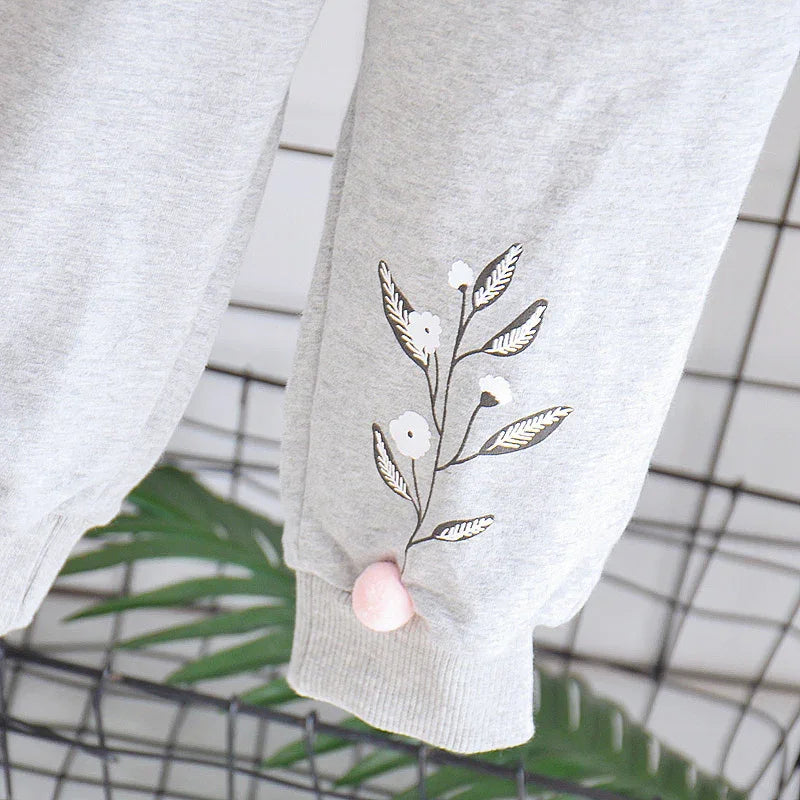 Light gray sweatpants with floral print and pink pom-pom detail on cuff