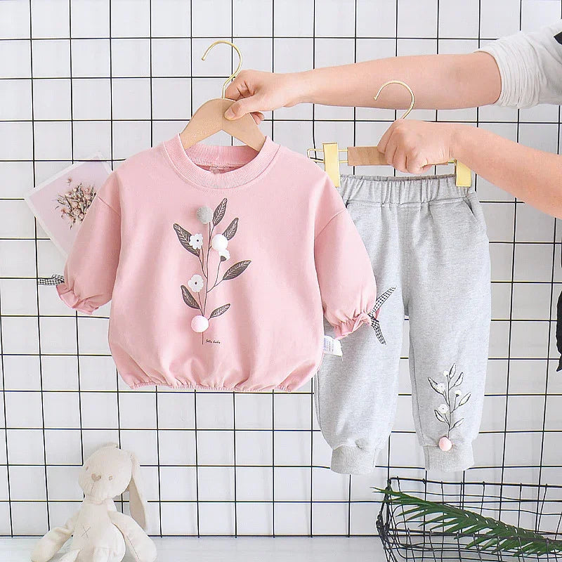 Pink floral embroidered toddler shirt with puffy sleeves and grey pants on hangers