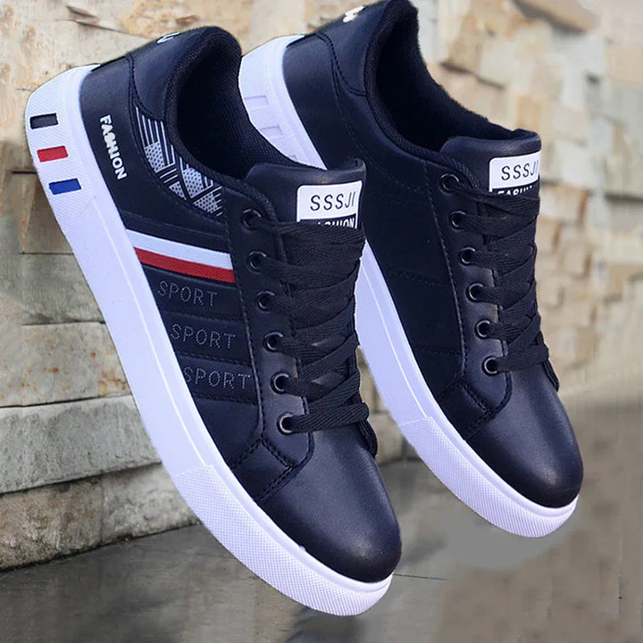 Black sport sneakers with white soles, red and blue stripes, and fashion details near a stone wall