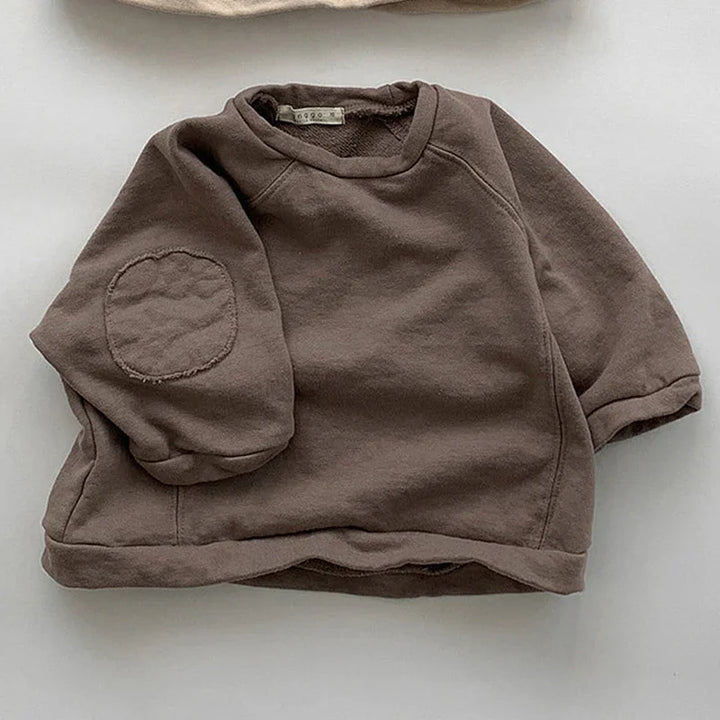 Brown toddler sweatshirt with round elbow patch on soft fabric background
