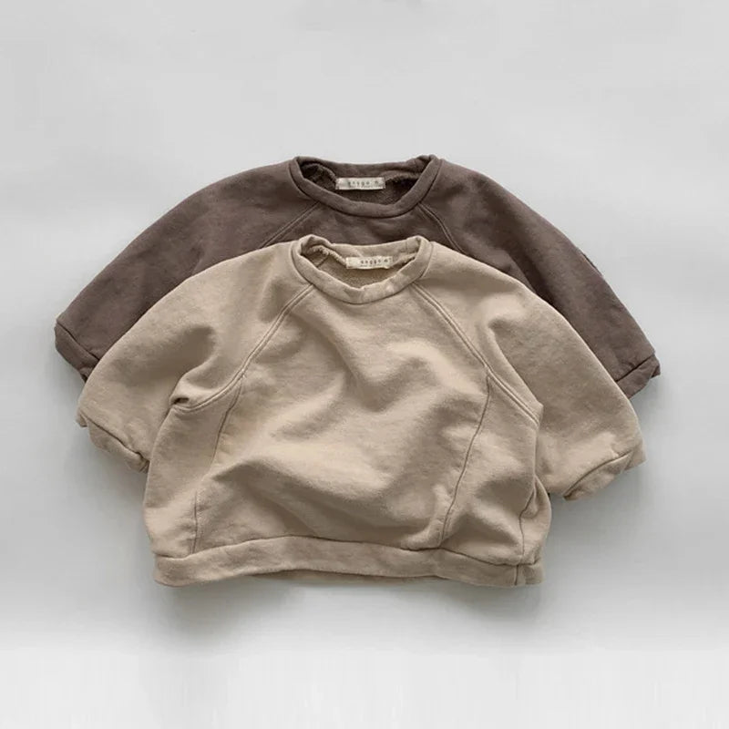 Two casual crewneck sweatshirts, one beige and one brown, laid flat on a white surface