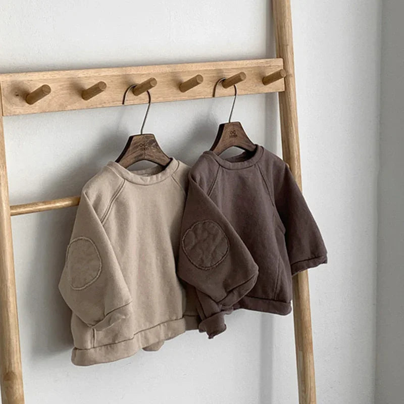Two casual sweatshirts in beige and dark brown with elbow patches hanging on wooden rack