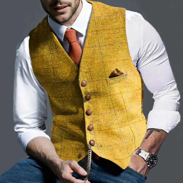 Man wearing yellow tweed vest with brown buttons, white shirt, orange tie, pocket square, and wristwatch