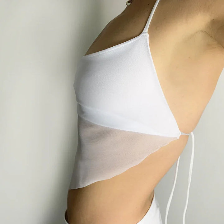 Side view of a person wearing a white asymmetrical crop top with thin straps and mesh fabric