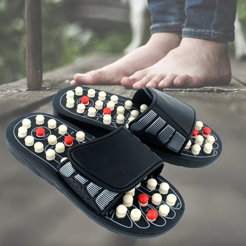 Black acupressure massage sandals with white and red pressure nodes on wooden floor near bare feet