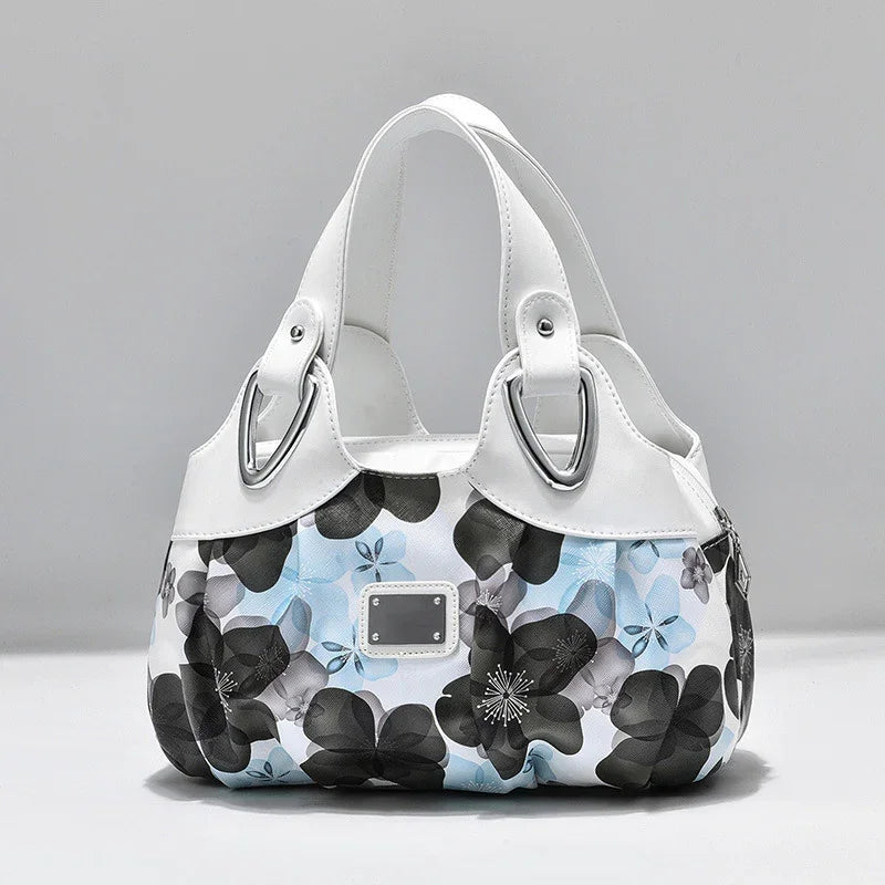 White handbag with blue and black floral pattern and silver hardware on white background