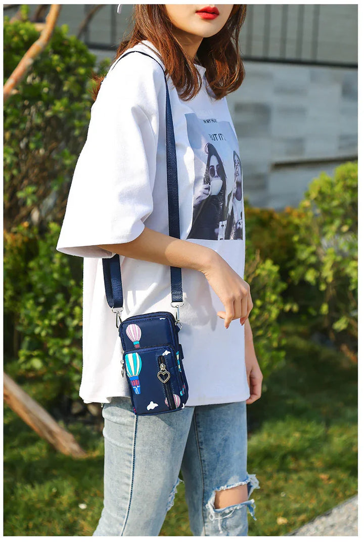 Woman wearing white graphic T-shirt and ripped jeans with navy crossbody bag featuring hot air balloon print