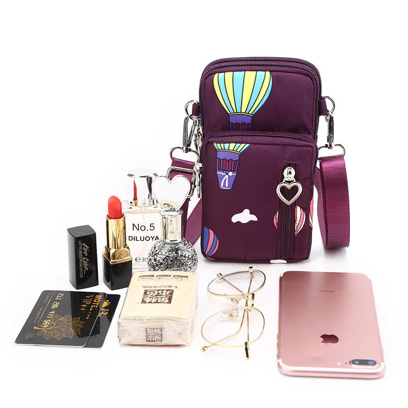 Purple crossbody bag with hot air balloon print, red lipstick, perfume, glasses, smartphone, tissue, and cards on white background