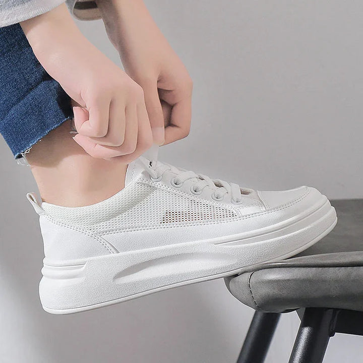 Person tying white mesh sneaker with elevated sole while resting foot on gray stool