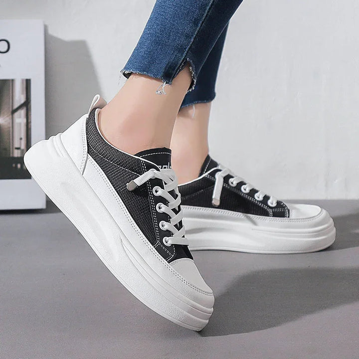 Black and white platform sneakers with white laces worn with frayed blue jeans on gray floor