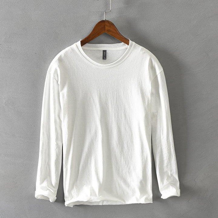 White long sleeve crew neck shirt hanging on wooden hanger against gray textured wall