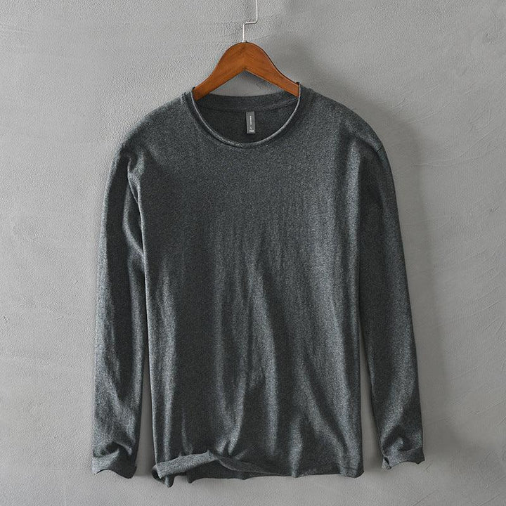Dark gray long sleeve crew neck shirt hanging on wooden hanger against gray textured wall