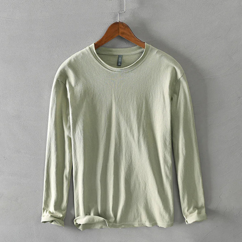 Light green long sleeve cotton shirt hanging on wooden hanger against gray wall