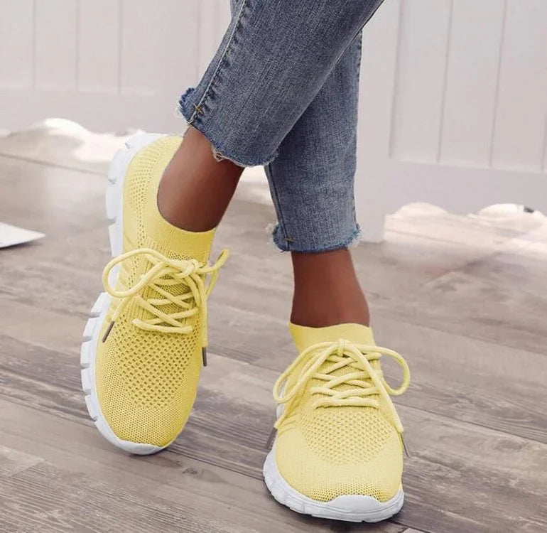 Yellow knit sneakers with white soles worn with cropped blue jeans on wooden floor