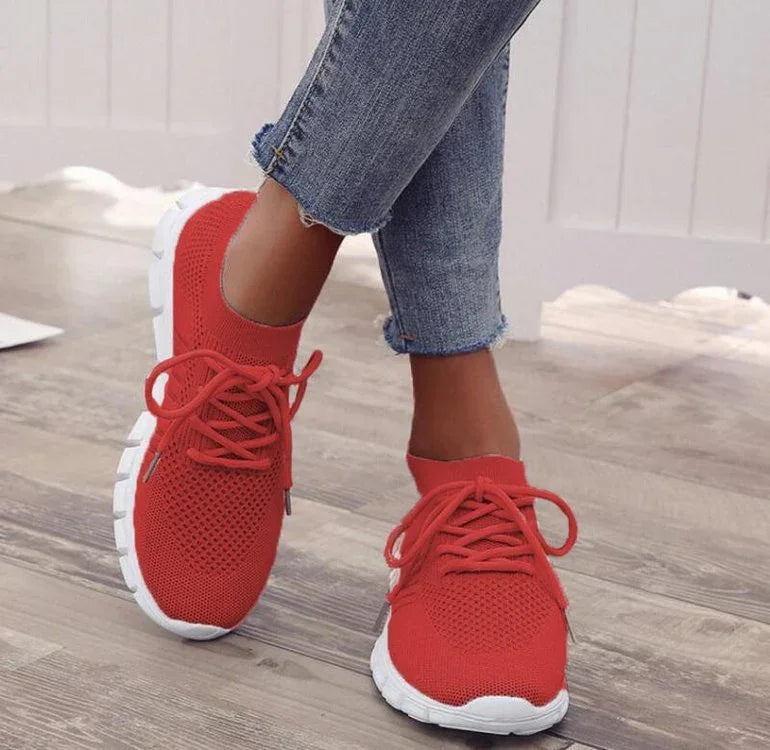 Close-up of feet wearing red knit sneakers with white soles paired with frayed blue jeans on wooden floor