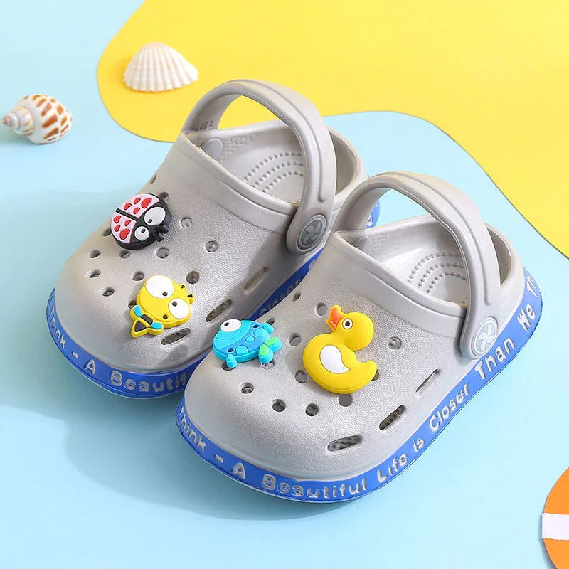 Gray children's clogs with blue soles featuring animal charms including ladybug, bee, turtle, and rubber duck toys