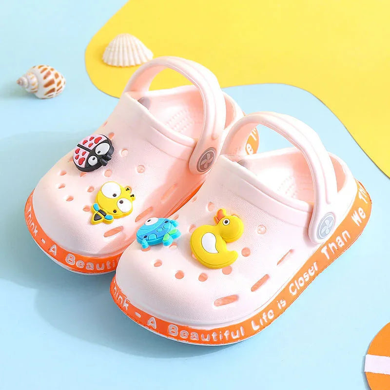 Pink children’s clog sandals with colorful animal charms and orange soles on blue and yellow background