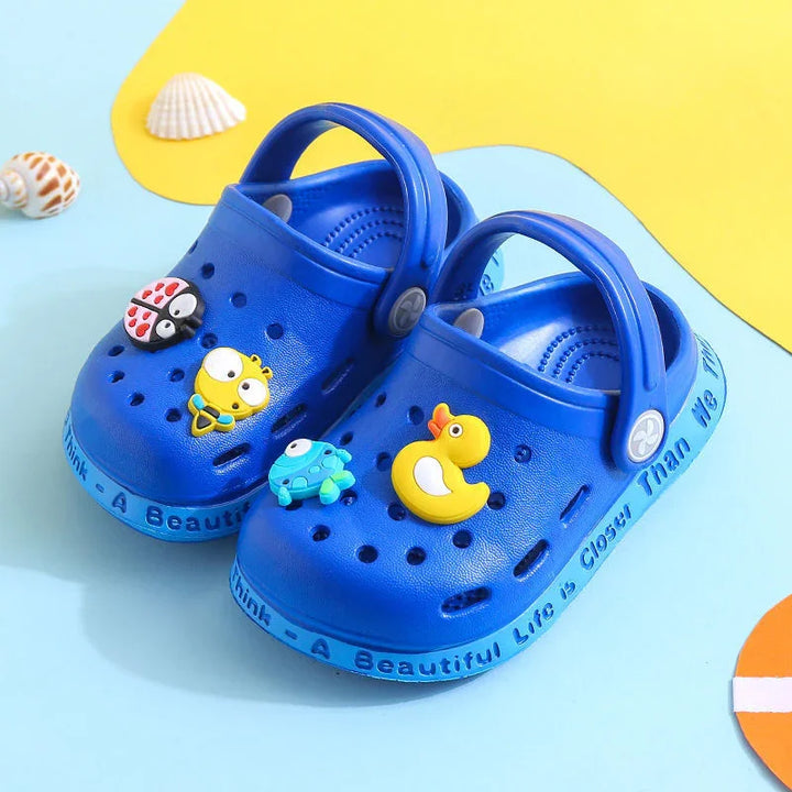 Blue kids clogs with colorful sea animal charms and quote along the sole on a bright background