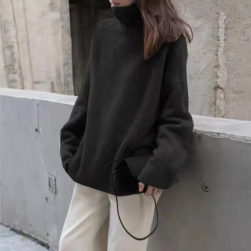 Woman wearing oversized black turtleneck sweater and beige pants leaning against concrete wall