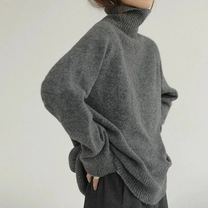 Woman wearing oversized grey turtleneck sweater with long sleeves against plain background