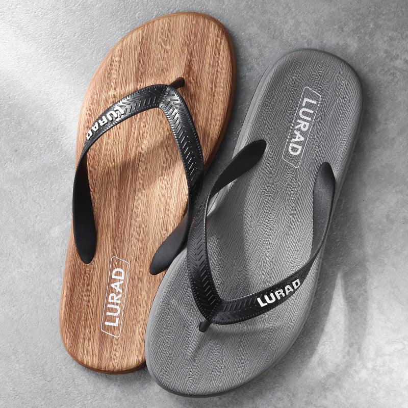 Pair of LURAD brand flip flops with wood texture sole and black straps on concrete background