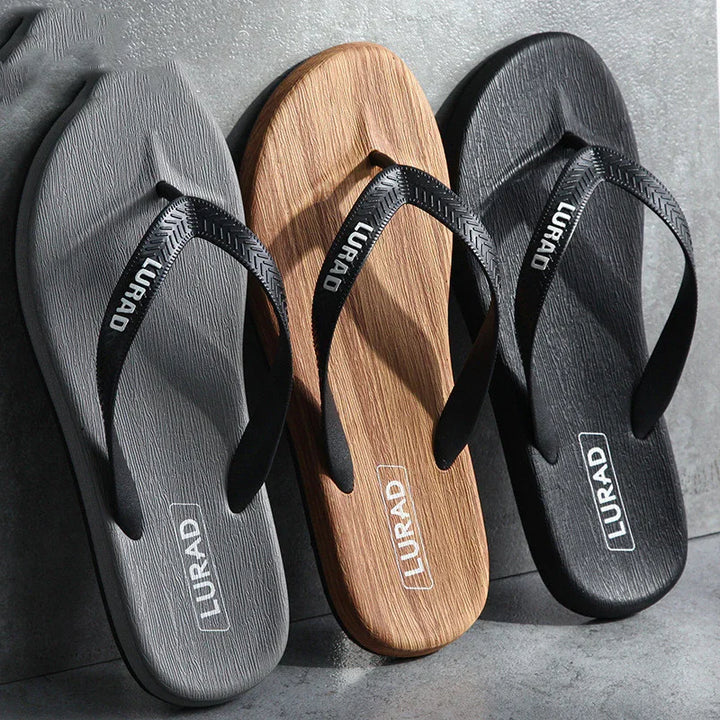 Three LURAD brand textured flip flops in gray, wood grain brown, and black on concrete surface