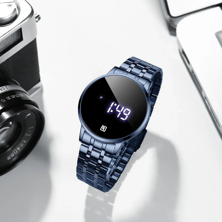 Modern blue stainless steel digital wristwatch showing 1:49 on black reflective face next to camera lens and laptop