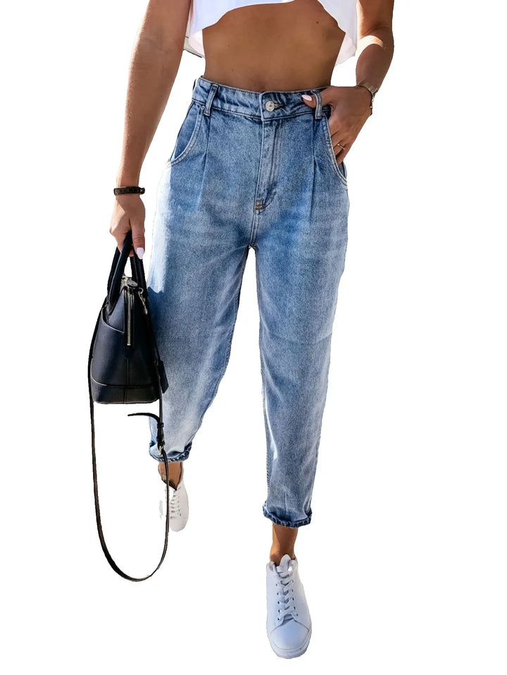 Woman wearing high-waisted light blue denim jeans with white sneakers and holding black leather handbag