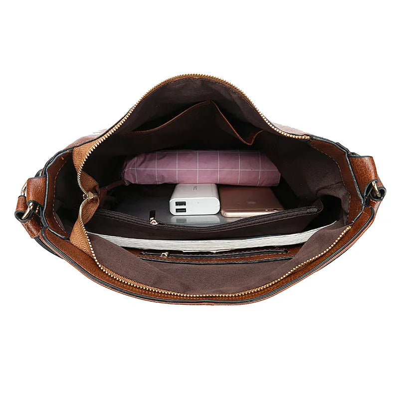 Open brown leather handbag showing organized interior with folded pink cloth, power bank, smartphone, and notebook