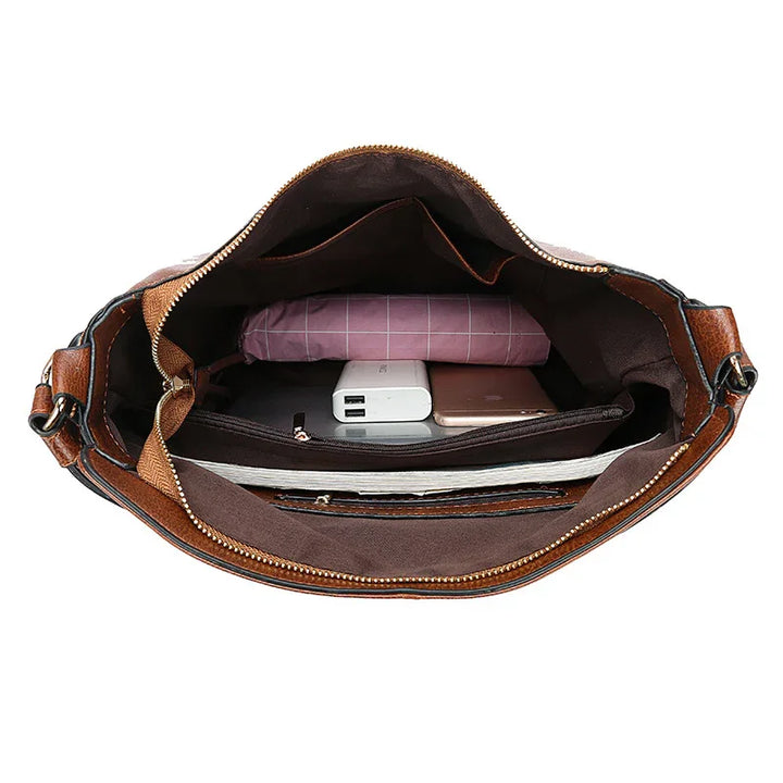 Open brown leather handbag showing organized interior with folded pink cloth, power bank, smartphone, and notebook