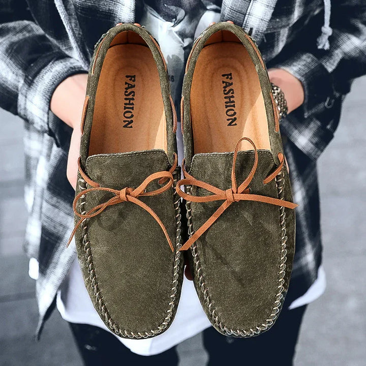 Close-up of men's casual suede loafers with brown leather laces held by person in plaid shirt